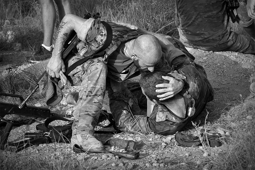 Two soldiers on the ground, one holding the other.